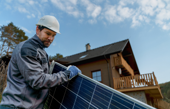 Solar panel installer wearing a hard hat and gloves working on a residential solar panel outside a home