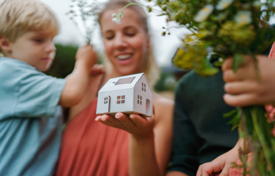 Mother and child holding a miniature model house with solar panels, representing energy-efficient homeownership.