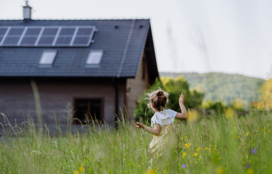 Young girl playing in a grassy field near a home with rooftop solar panels.